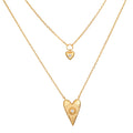 Two-layered gold necklace set with small heart pendant and larger textured heart pendant, each with central crystal stone.