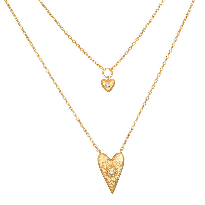 Two-layered gold necklace set with small heart pendant and larger textured heart pendant, each with central crystal stone.