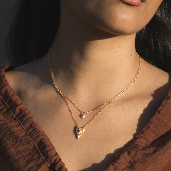 Two-strand gold necklace set with small heart and pointed crystal pendants worn layered on model.
