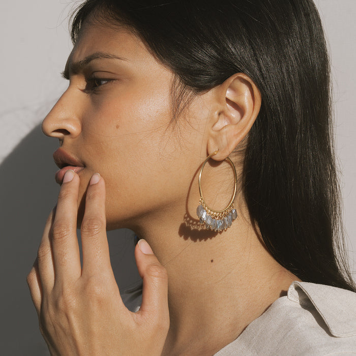 Gold hoop earrings with iridescent labradorite beads dangling below, worn on model with long dark hair.