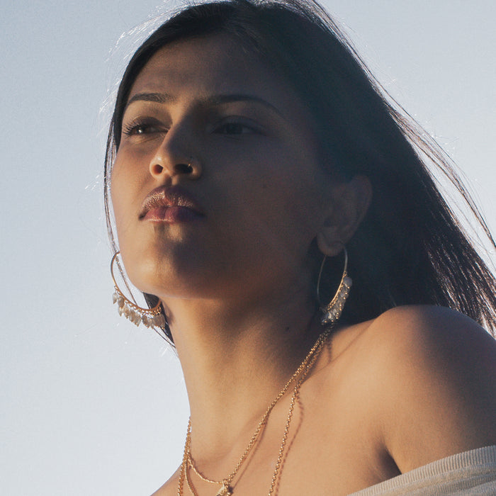 Gold-toned hoop earrings with labradorite stone accents worn on a person's ears.