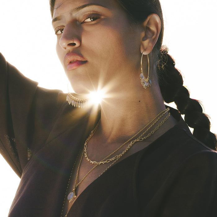 Gold-toned hoop earrings with labradorite stone drops worn on a person's ears.