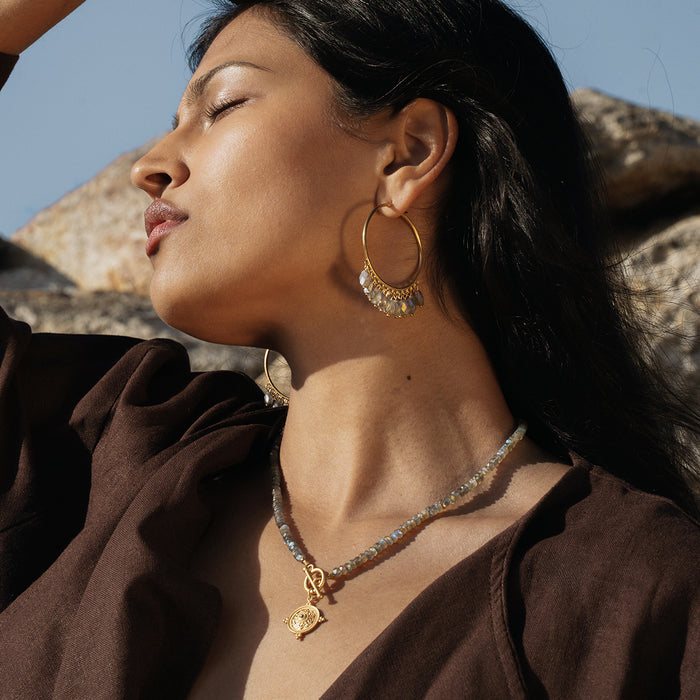 Gold hoop earrings with labradorite and pearl beads worn by a woman in profile.