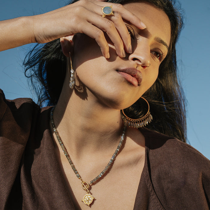 Gold-toned toggle necklace with labradorite stone pendant and beaded chain worn on model against blue background.
