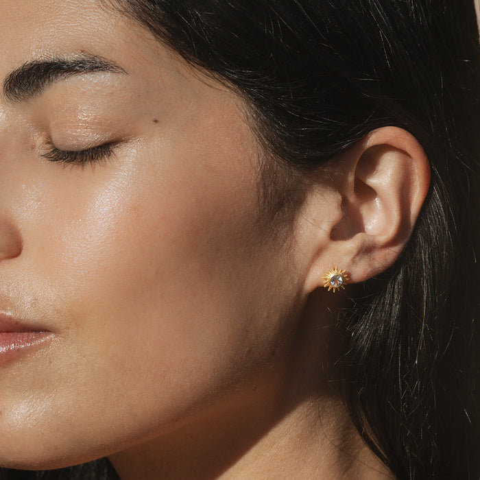 Close-up of a model wearing Light Seeker White Topaz Starburst Stud Earrings, highlighting the golden starburst pattern and white topaz stone. This spiritual jewelry piece serves as a talisman for yoga practitioners, amplifying the powers of manifestation and spirituality while embodying the essence of sun and moon energy.