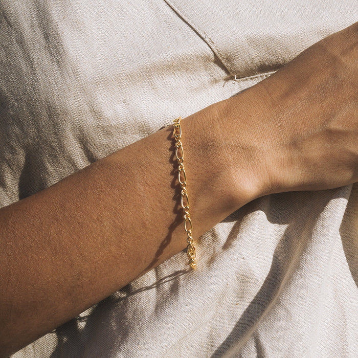 Gold-toned chain bracelet with linked oval loops worn on wrist against neutral fabric.