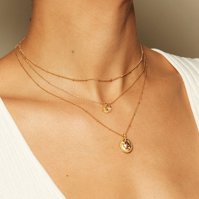 The Lotus Pink Tourmaline Birthstone Locket Necklace - October layered with other necklaces on a model, representing the essence of spiritual jewelry, charm, and zodiac meanings for a chic, meaningful look.