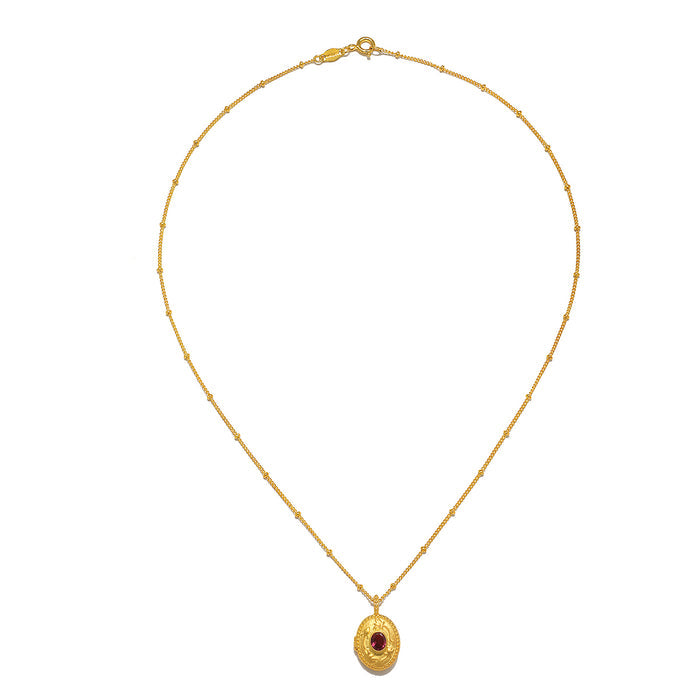The Lotus Pink Tourmaline Birthstone Locket Necklace - October laid flat against a white surface, showcasing the gold plating, design, and its significance as a talisman for protection and introspection.