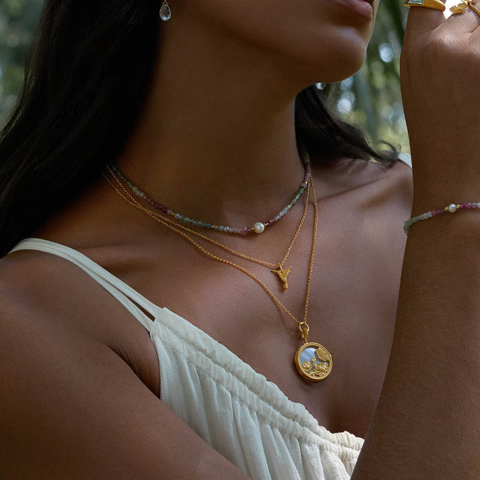 A woman showcasing layered necklaces including the Loving Devotion Hummingbird Necklace, embodying the essence of spiritual and meaningful jewelry. Perfect for meditation and yoga, this talisman represents manifestation and the connection to the sun and moon.