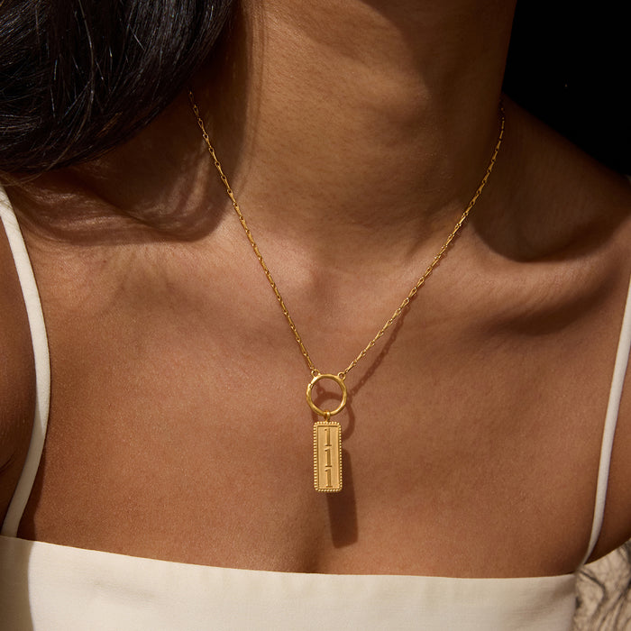 Gold-toned rectangular pendant with "111" engraved on face, hanging from delicate chain worn as necklace.
