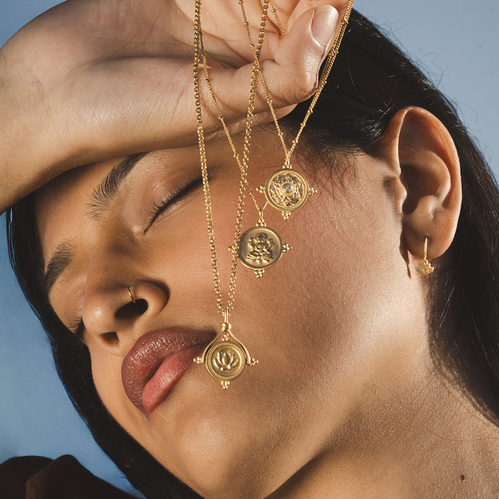 Three gold-toned pendant necklaces with circular coin charms featuring lotus and deity designs on chain links.