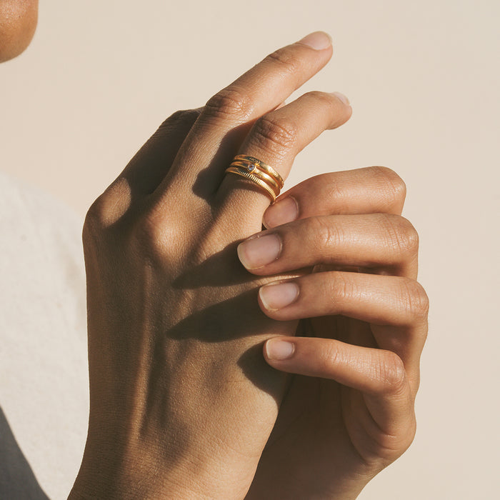 Gold-toned adjustable ring with white topaz stone worn on middle finger of hand.