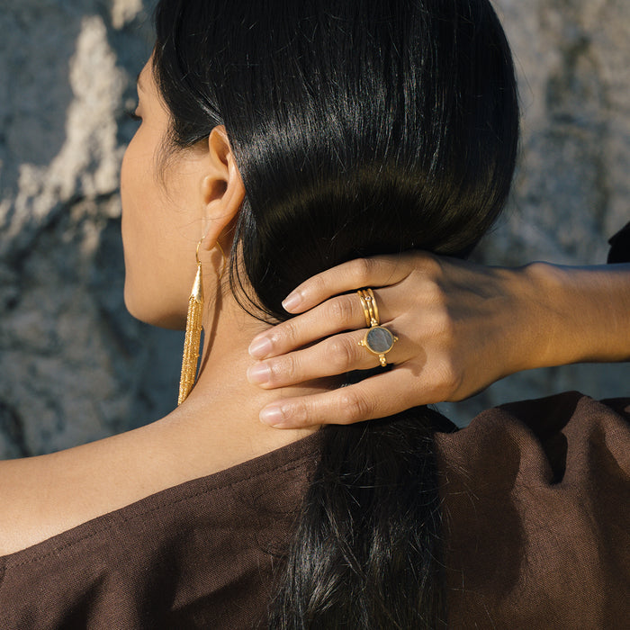 Gold-toned adjustable ring with round clear stone worn on finger with matching gold earrings.
