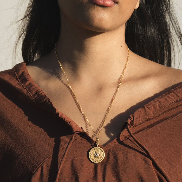 Gold-toned coin pendant necklace with detailed circular design worn on delicate chain.