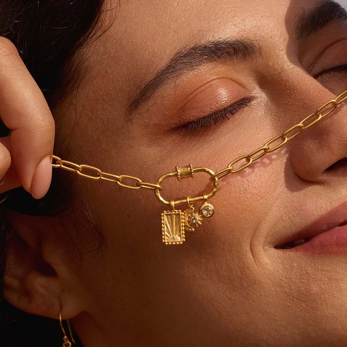 A close-up of the New Beginnings Lotus Charm Holder Necklace worn by a model, showcasing its elegant design featuring a carabiner charm holder. This spiritual jewelry piece represents transformation and renewal, perfect for yoga and meditation practices. Its gold plating punctuates the meanings of protection and manifestation.