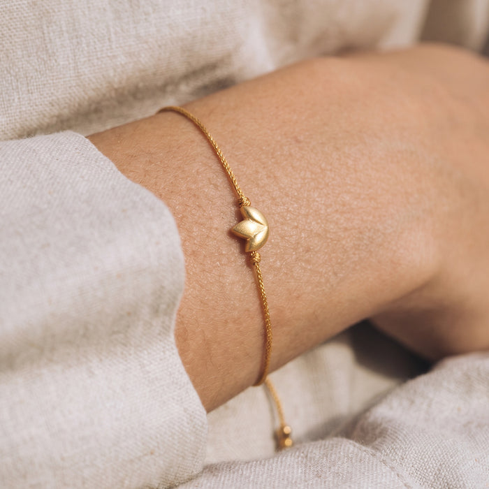 Gold lotus charm bracelet with thin cord strap worn on wrist.