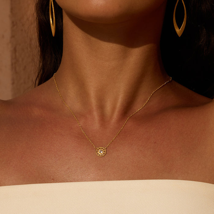 Gold-tone necklace with small circular sun pendant worn on person's chest.
