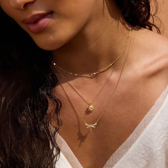 Gold-toned necklace with layered chains and a star-shaped crystal pendant worn on person's neck.