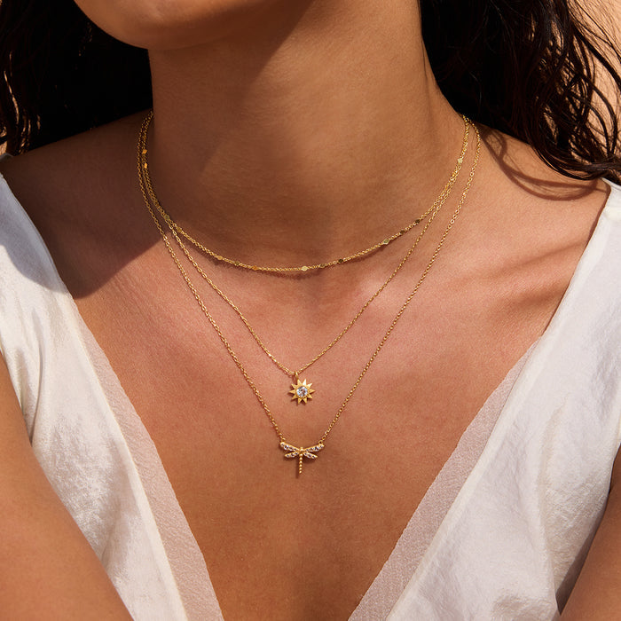 Gold-toned layered necklaces with sun and dragonfly pendants worn on model's neck.
