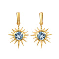 Pair of gold starburst earrings with blue topaz gemstones at the center and pointed rays radiating outward.
