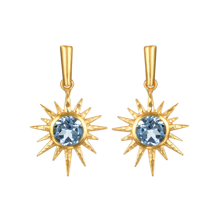 Pair of gold starburst earrings with blue topaz gemstones at the center and pointed rays radiating outward.