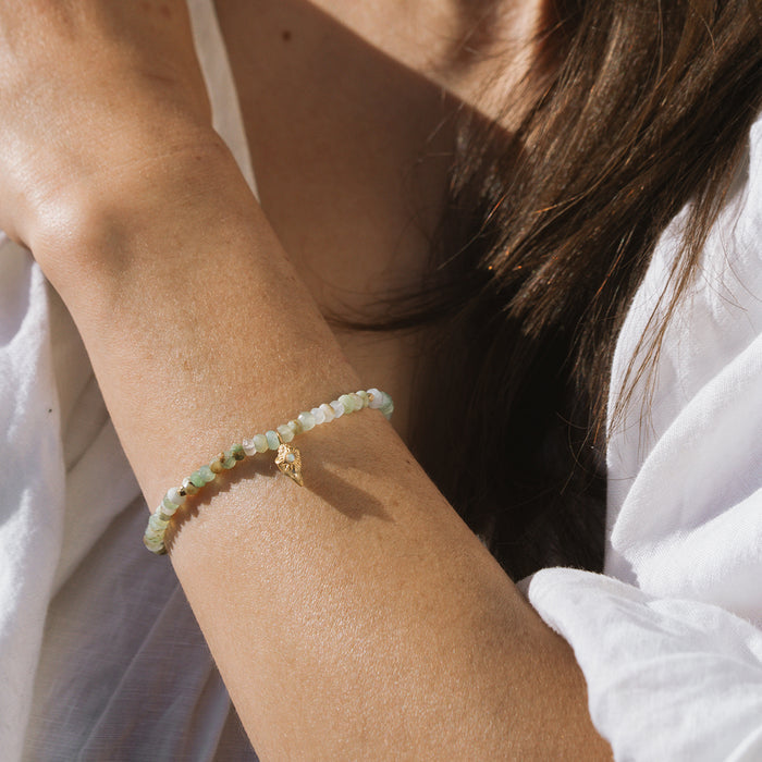 Beaded bracelet with pale green and white opal stones worn on wrist with gold-tone charm detail.