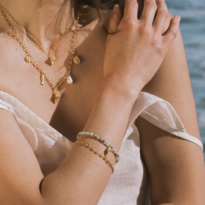 Gold bracelet with pale green shell opal beads and gold chain links worn on wrist.