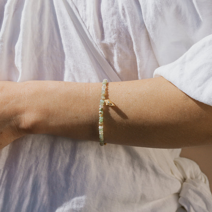 Beaded bracelet with pale green and white stones worn on wrist over white linen sleeve.