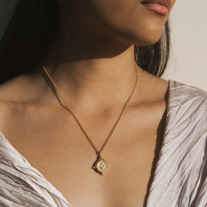Gold-toned necklace with circular lotus-engraved pendant and spinning detail worn at chest level.
