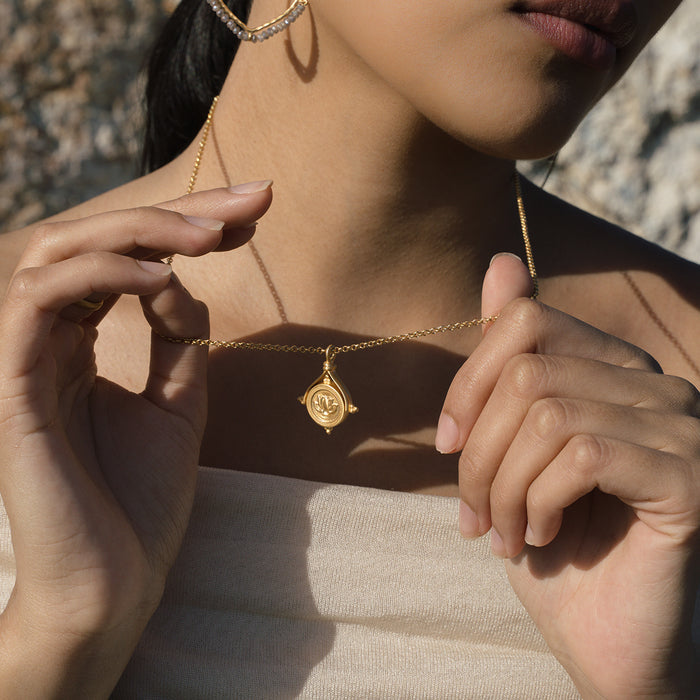 Gold-toned spinner necklace with oval labradorite pendant and lotus engraving, worn on person.