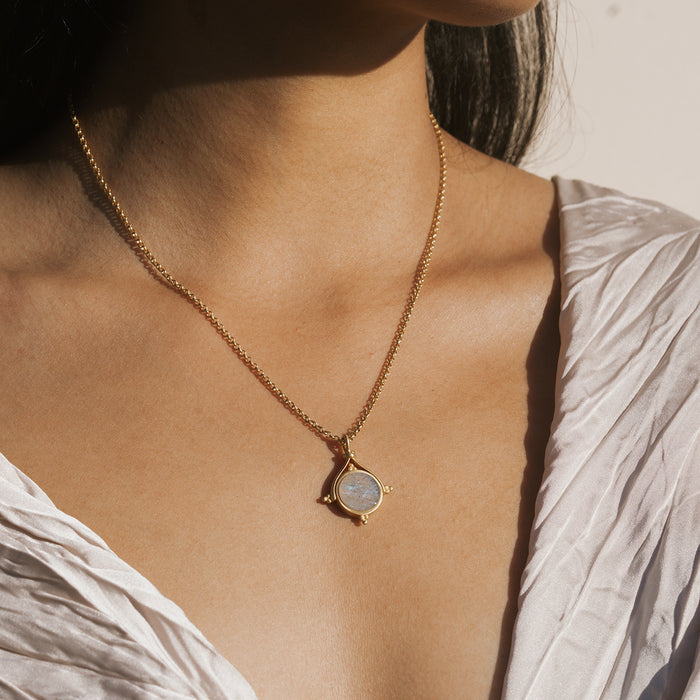 Gold-tone necklace with labradorite stone pendant suspended from delicate chain, worn on person's chest.