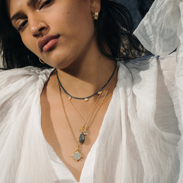 Layered necklaces with dark beaded chain and gold chains featuring labradorite stone pendants worn on model.