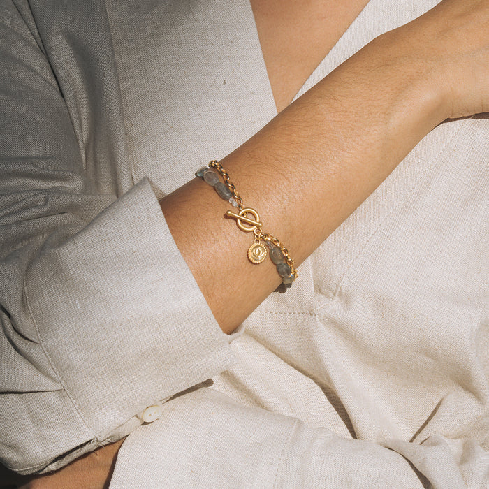 Gray labradorite beaded bracelet with gold toggle clasp and lotus charm pendant worn on wrist.