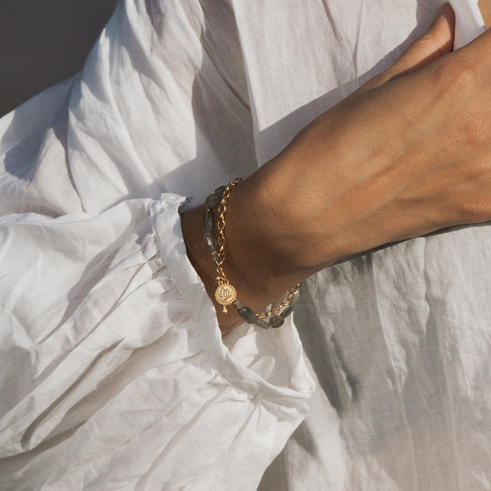 Gold-tone chain bracelet with labradorite stone and lotus toggle clasp worn on wrist.
