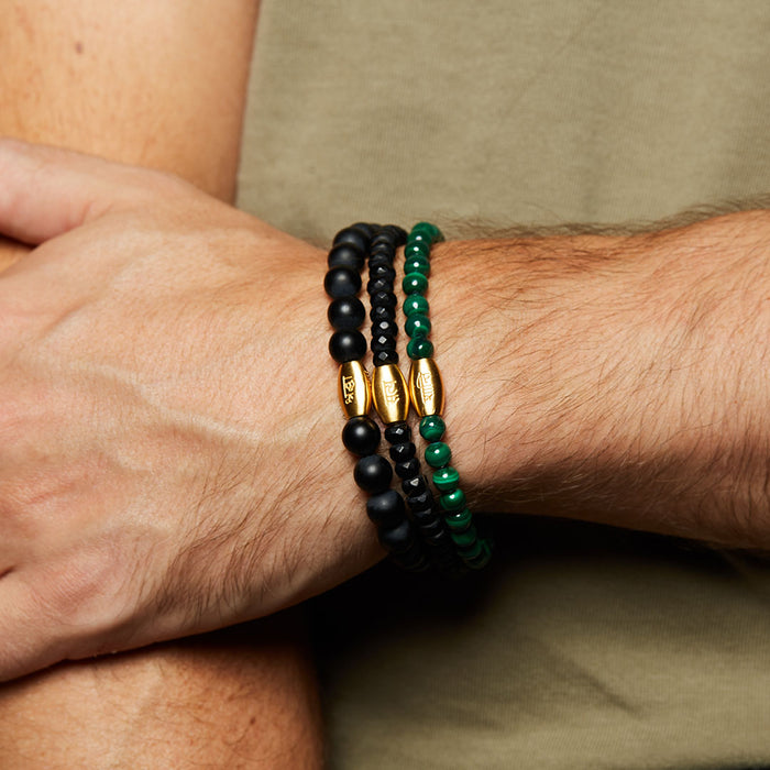 Close-up of the Path to Healing Malachite Gemstone Men's Bracelet paired with other beaded bracelets, featuring messages of truth and peace. This combination represents a powerful embodiment of spiritual and meaningful jewelry used in meditation and manifestation.