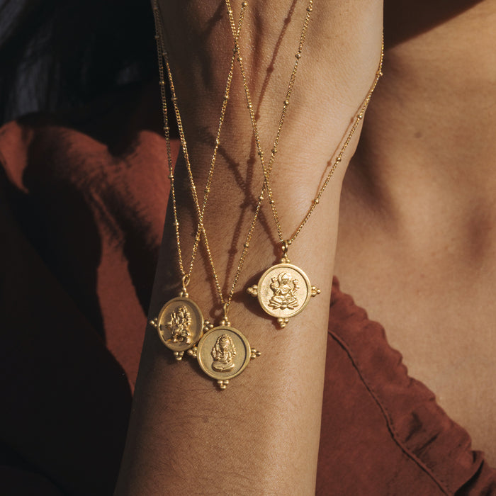 Gold chain necklaces with round Ganesha medallion pendants worn layered on wrist.