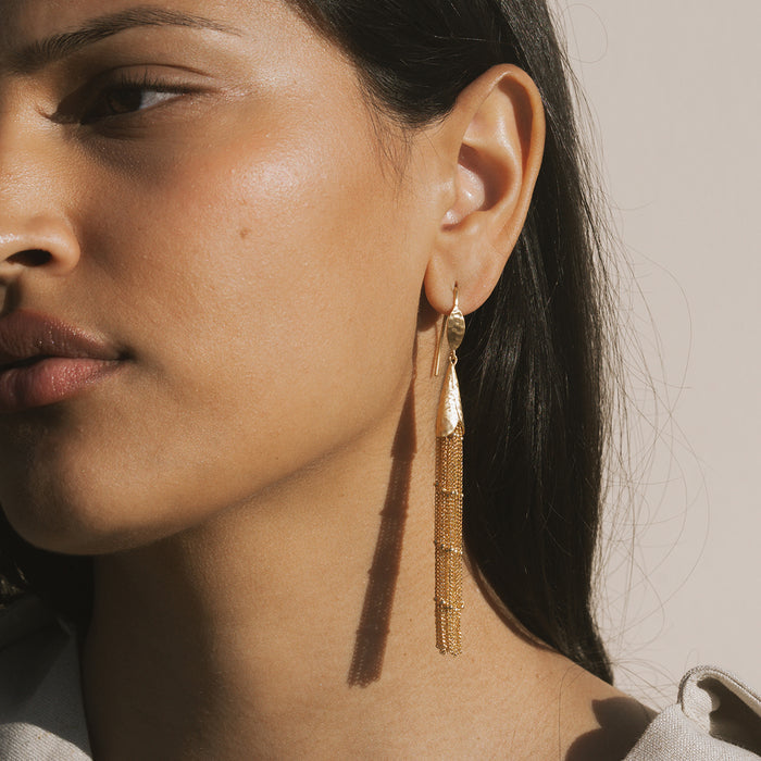 Gold-tone tassel earrings with chain details hanging from ear wires on a model.