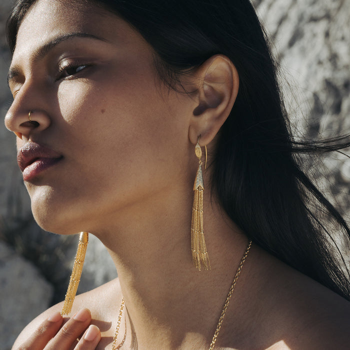 Gold-toned tassel earrings with beaded details hanging from small circular studs on a woman's ears.