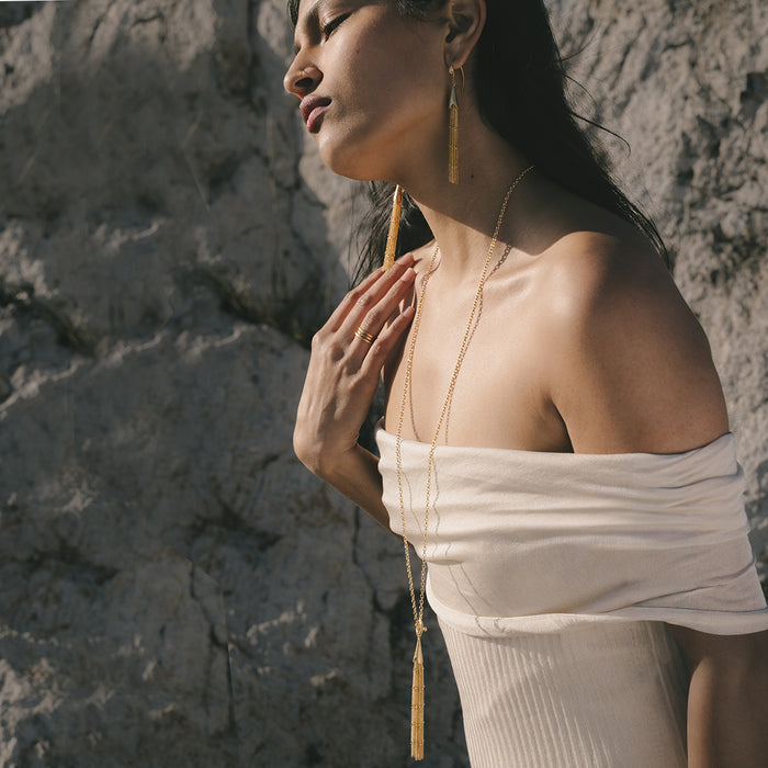 Gold-tone chain necklace with black and gold tassel toggle pendant, worn layered on model.