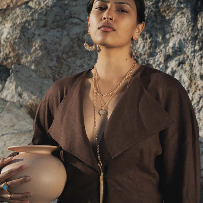 Gold-toned chain necklace with toggle clasp and tassel pendant worn over brown shirt.