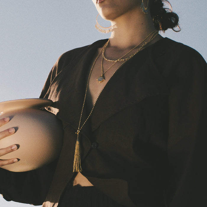 Gold-tone layered chain necklace with tassel toggle pendant worn layered on model in black shirt.