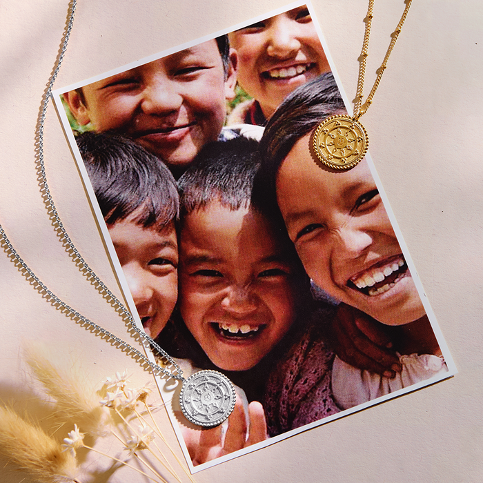 Gold and silver circular pendant necklaces displayed with a photo of smiling children and dried flowers on neutral background