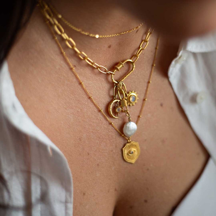 Gold layered necklaces with pearl and geometric charm pendants worn on neck.