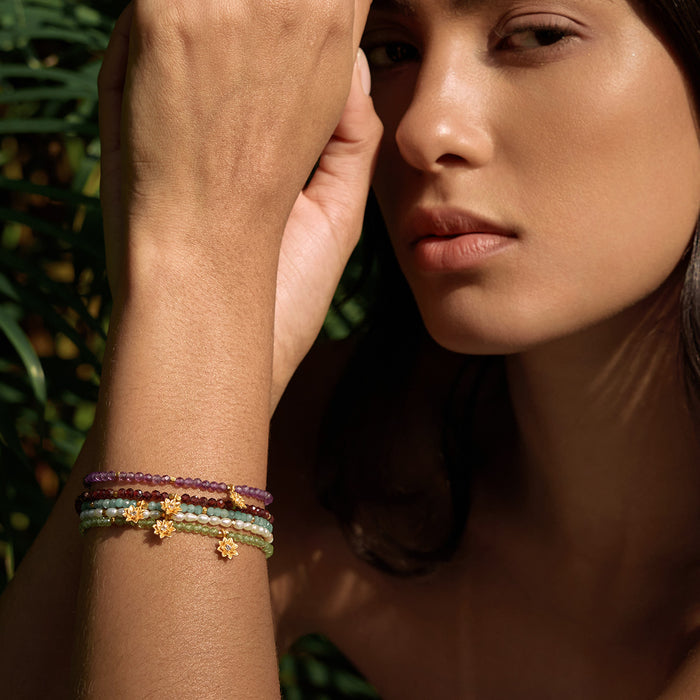 Stacked beaded bracelets with red garnet, gold accents, and green stones worn on wrist.