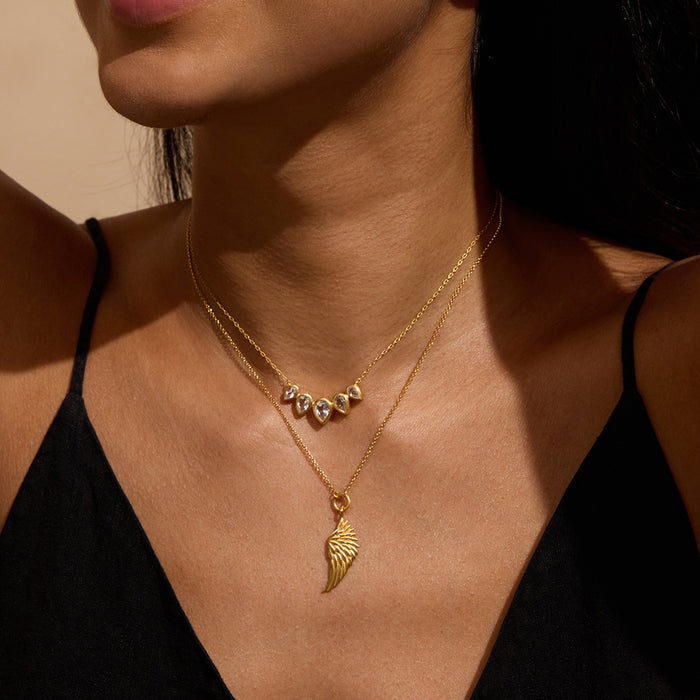 Gold-tone layered necklace with angel wing pendant and decorative beaded chain worn on model's neck.