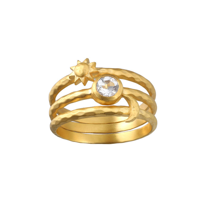Three-piece gold ring set with sun motif, circular crystal stone, and textured bands stacked together.