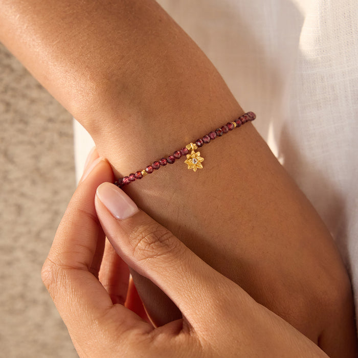 Bracelet with deep red round beads and small gold lotus flower charm worn on wrist.