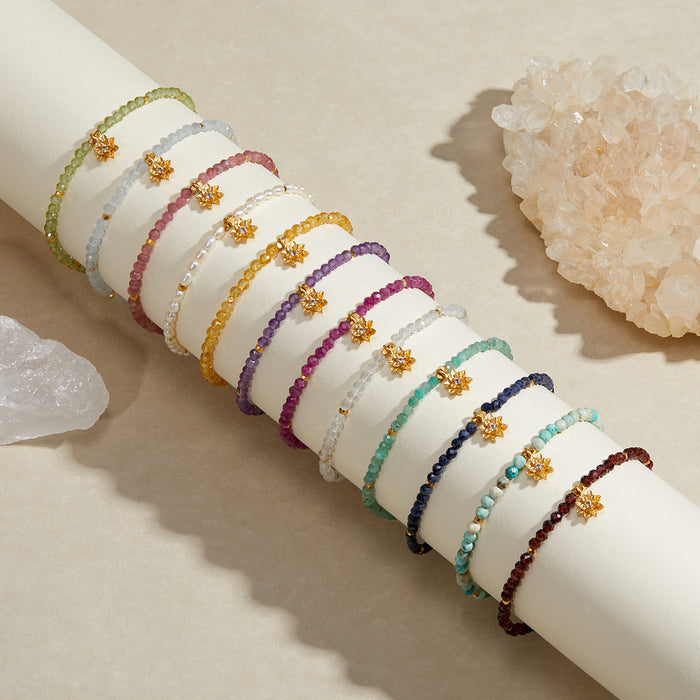 Collection of beaded bracelets in various colors with small gold lotus charms, displayed on a white cylinder with crystals.