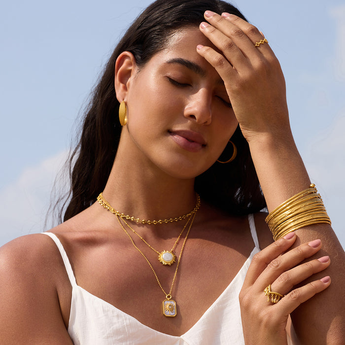 Gold-toned necklace with layered chains and mother of pearl sun pendant worn with matching gold jewelry.