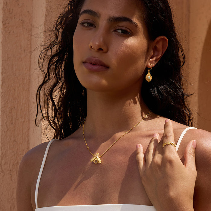 Gold-toned necklace with small faceted crystal pendant worn on model with matching earrings and ring.